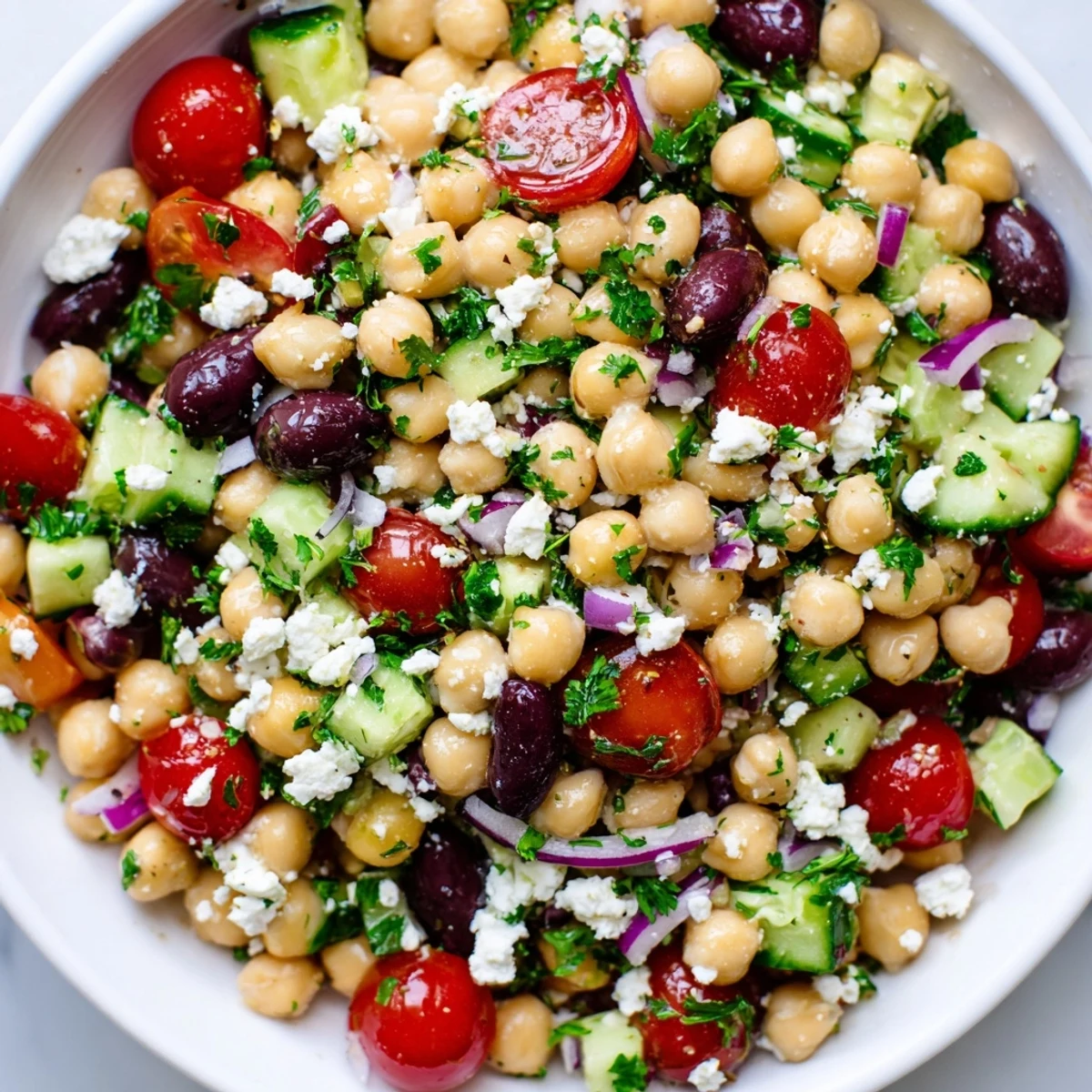 A vibrant Mediterranean Chickpea Salad with Feta in a white bowl, topped with crumbled cheese and fresh parsley for a refreshing summer side dish.  