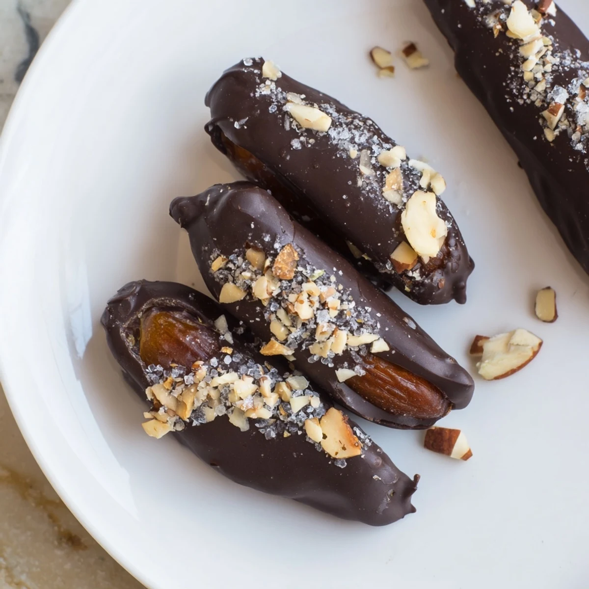 A close-up of Chocolate Covered Dates Stuffed with Almond Butter, topped with chopped nuts, showing creamy filling on a baking sheet.