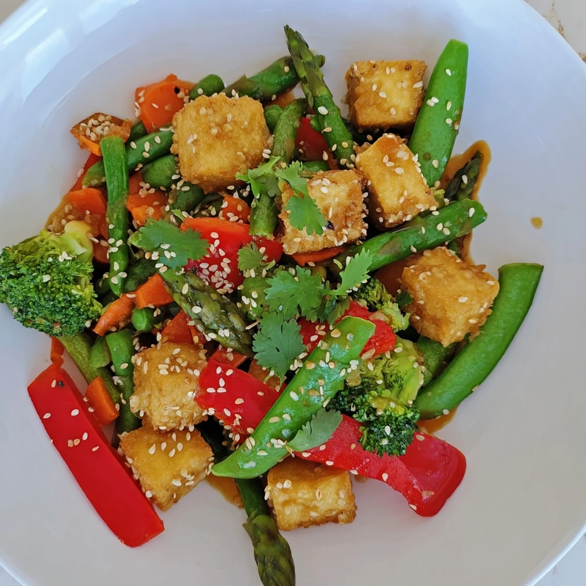 Healthy vegan Spring Vegetable Stir Fry with Tofu, garnished with sesame seeds and fresh herbs on a wooden table.