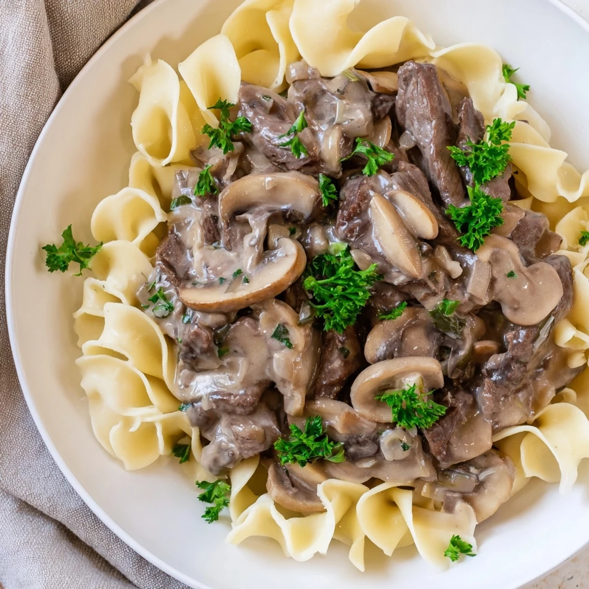 Savory Beef Stroganoff with Egg Noodles served in a bowl, garnished with fresh parsley and sautéed mushrooms.