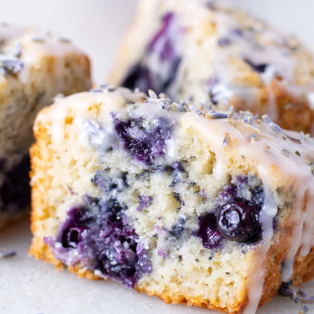 A plate of Lavender Blueberry Tea Cakes with a lemon glaze, served beside a steaming cup of Earl Grey tea.