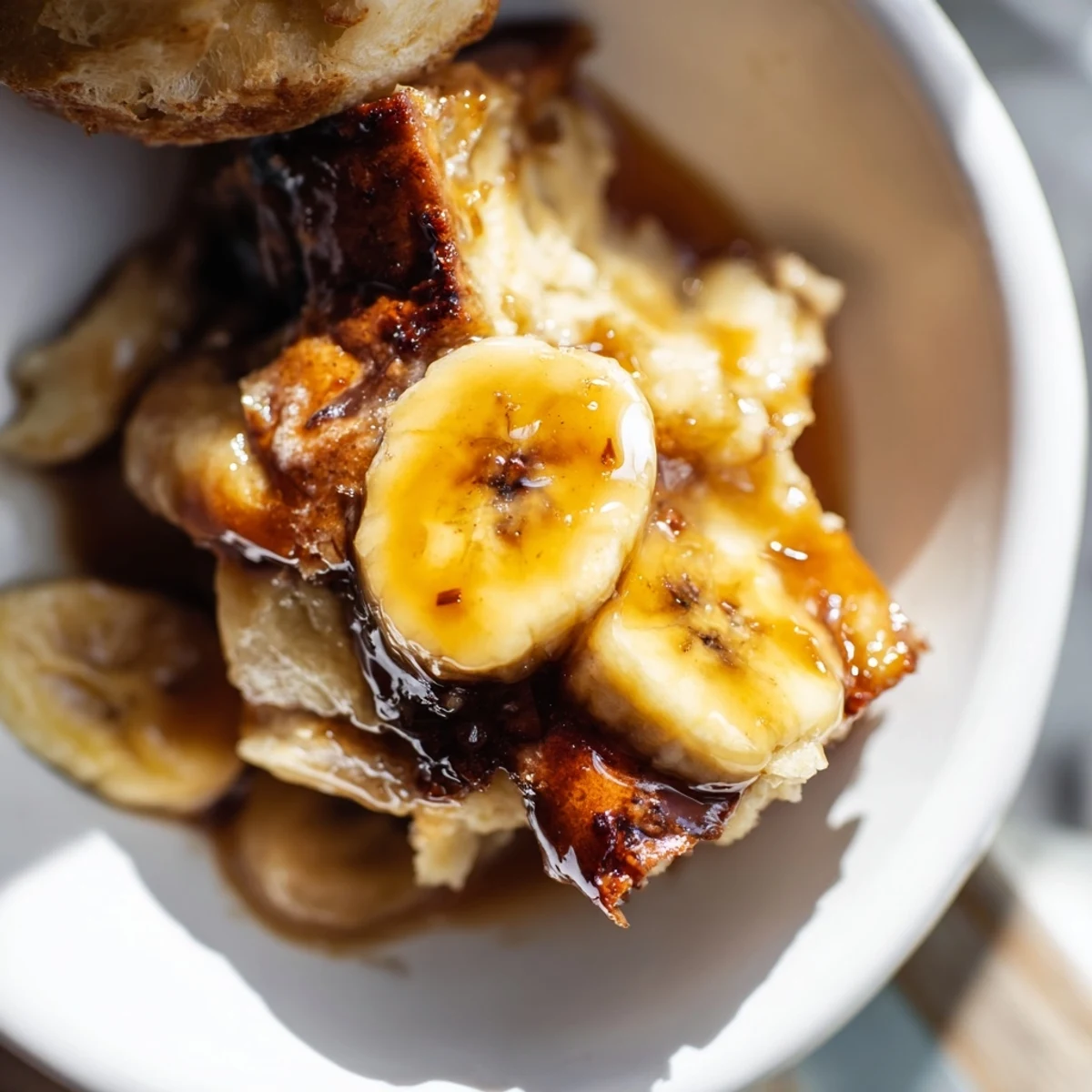 Creamy Bananas Foster Bread Pudding glistens with rum-butter sauce on a white plate, golden caramelized bananas visible.