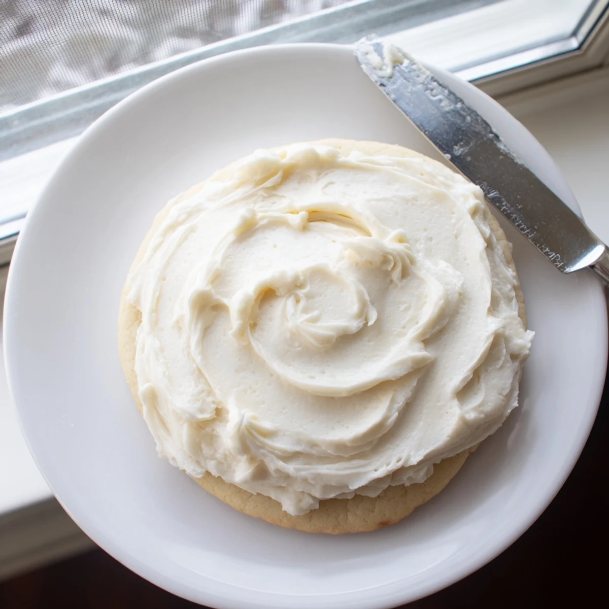 Easy Sugar Cookie Frosting in pastel colors decorates festive cookies with a soft glossy finish on a white plate.