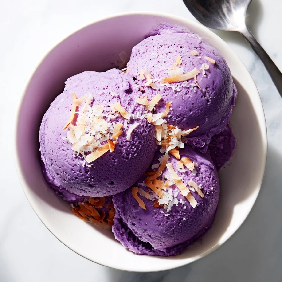 Perfectly scooped Ube Ice Cream topped with toasted coconut, ready to serve on a sunny patio table.