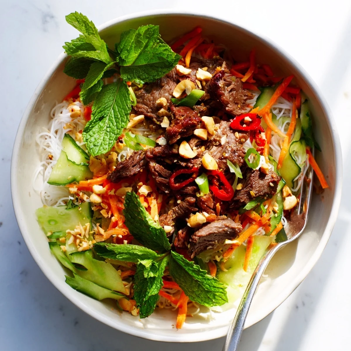 Fresh Bun Bo Xao in a bowl, sautéed beef and crisp veggies over noodles with nuoc cham drizzle.