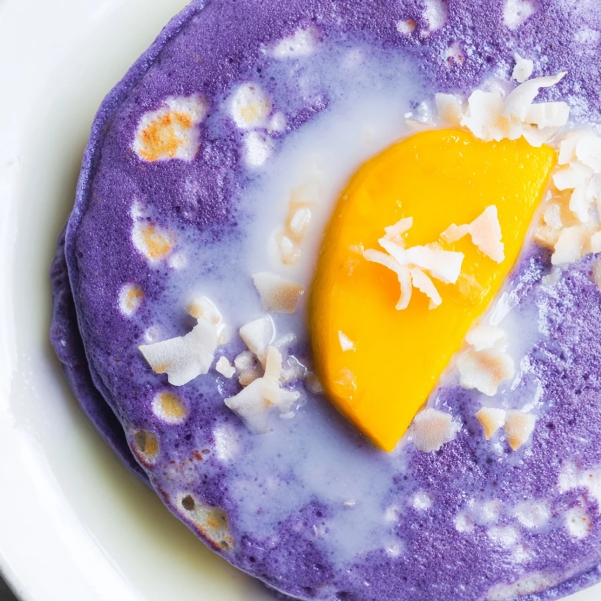 Soft, sticky Ube Mochi Pancakes drizzled with sweetened condensed milk and fresh mango slices.
