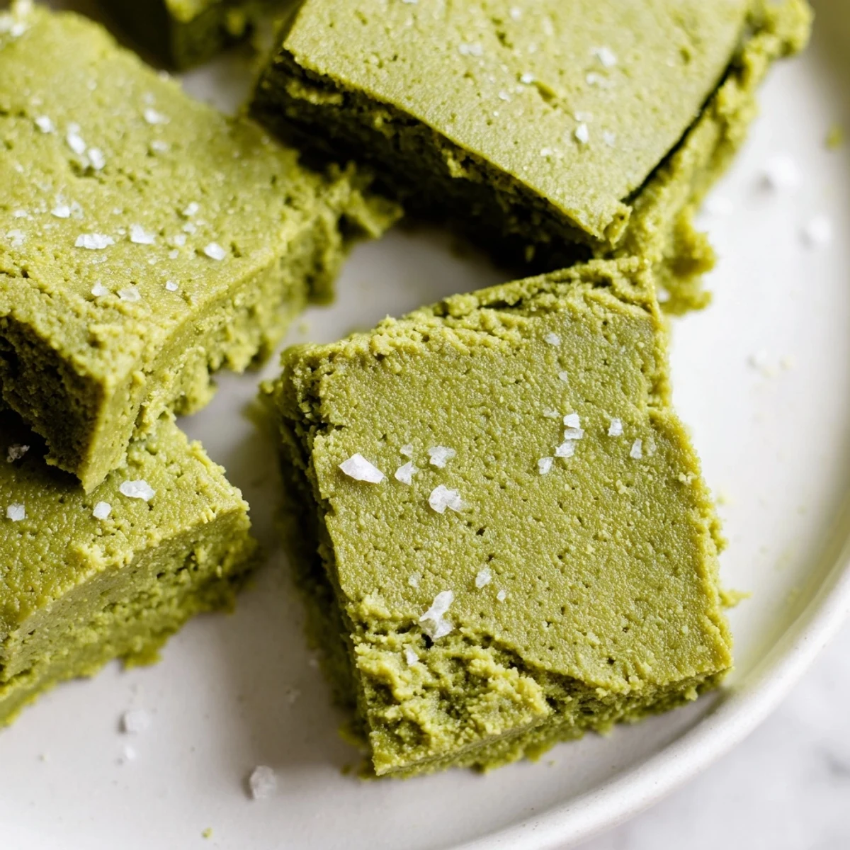 The finished 5-Ingredient Matcha Halva is cut into cubes on a marble countertop, showing the crumbly texture and vivid matcha color.