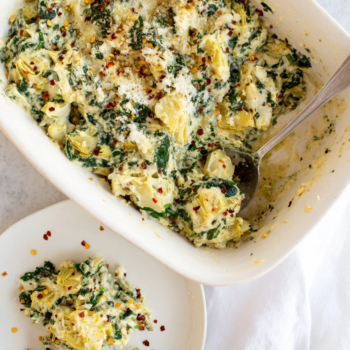 Golden baked spinach artichoke dip topped with bubbly cheese, alongside sliced baguette and colorful vegetable sticks for dipping.