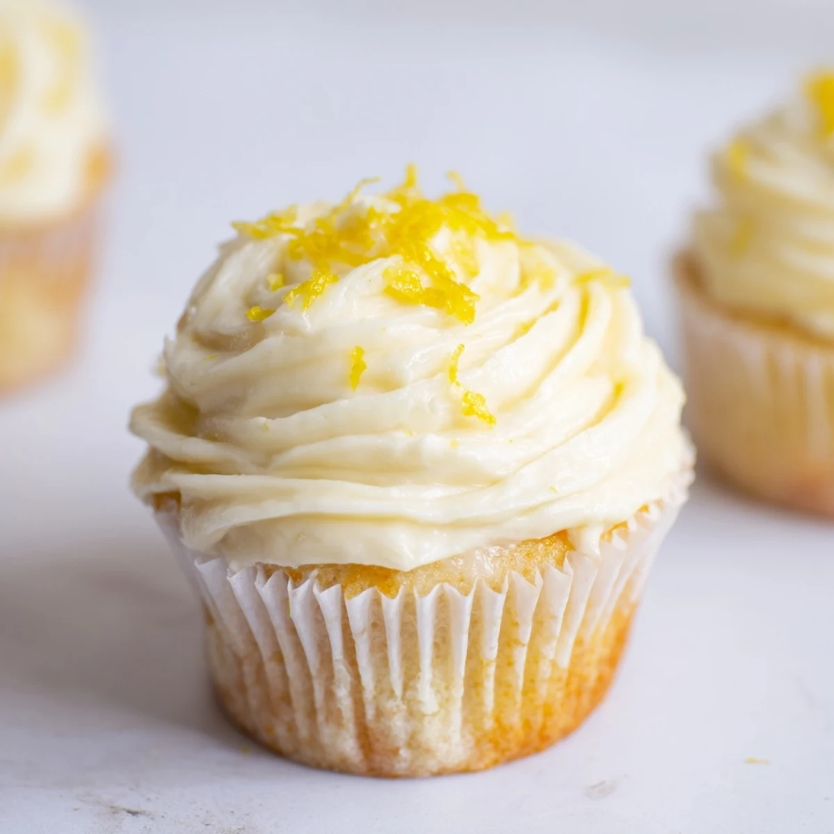 Moist Limoncello cupcakes with creamy frosting are arranged on a white plate beside a glass of Italian liqueur.