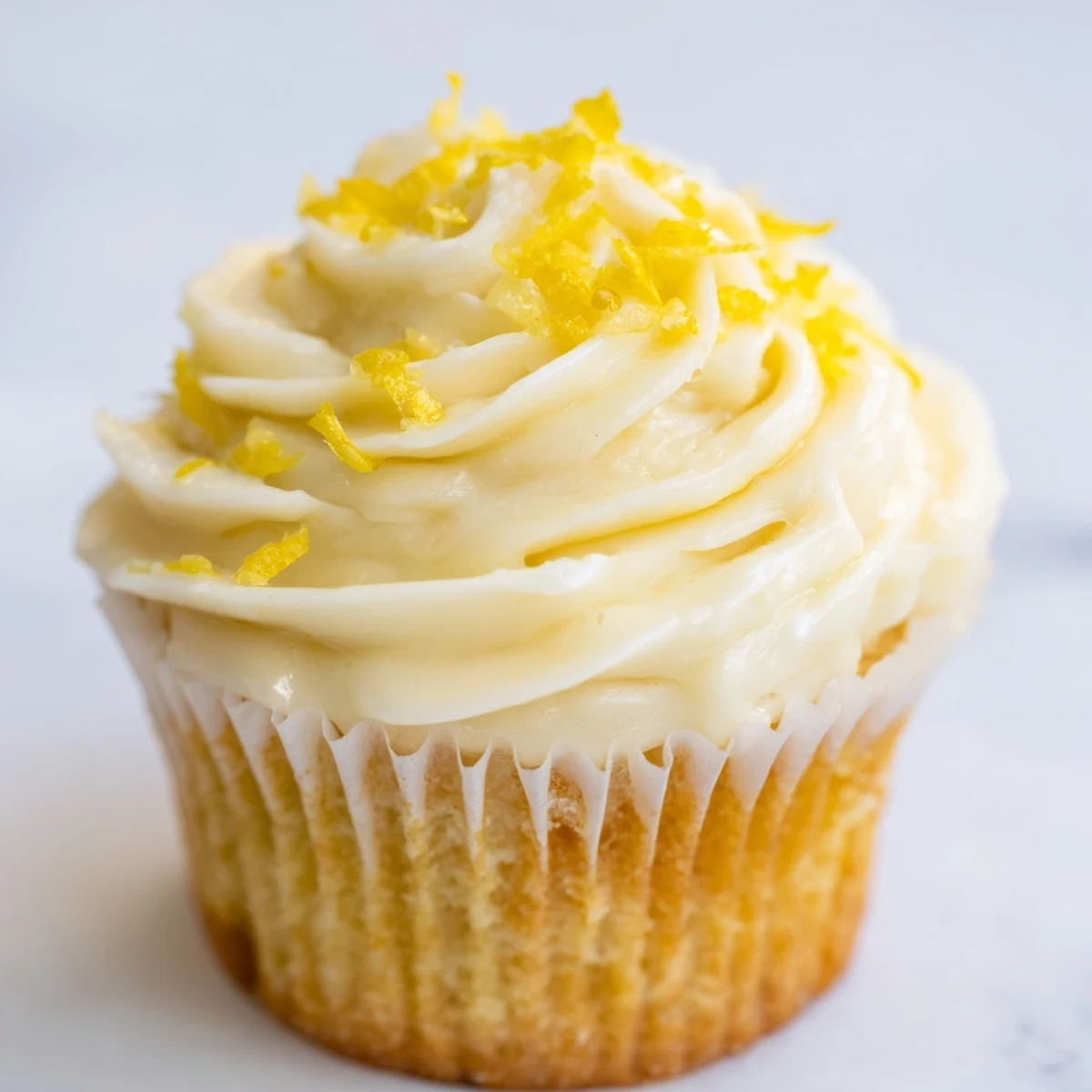 Perfect for summer gatherings, Limoncello cupcakes sit on a marble counter with fresh lemons and blooming flowers nearby.