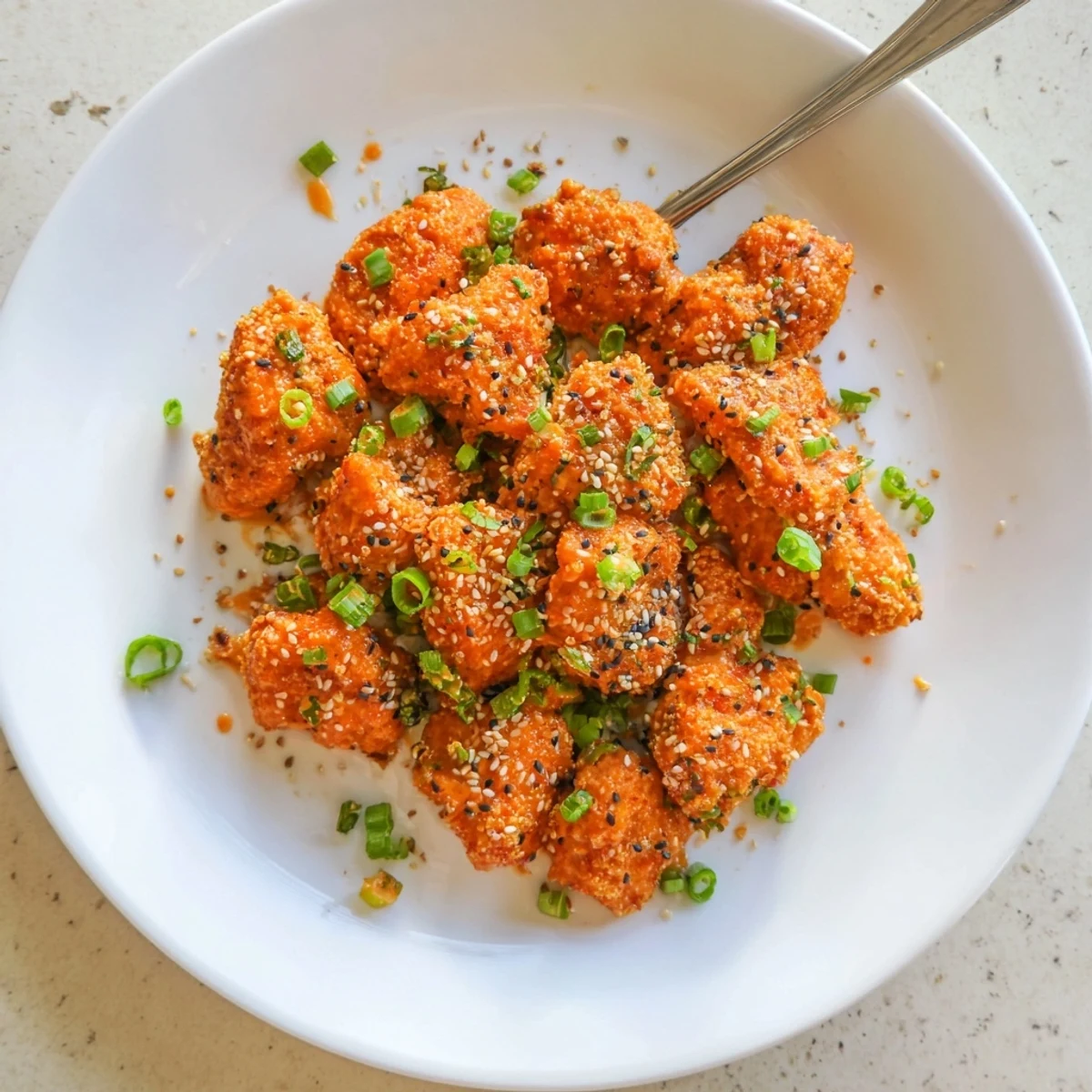 Golden brown chicken bites coated in almond flour and parmesan, glistening with creamy bang bang sauce and topped with fresh scallions and sesame seeds.