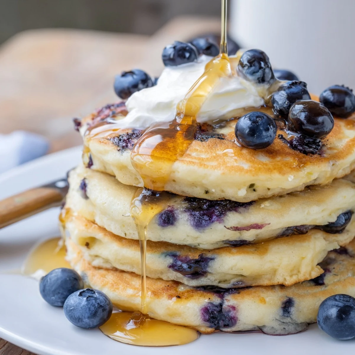Fluffy Greek yogurt blueberry pancakes stacked high with fresh berries and maple syrup drizzle