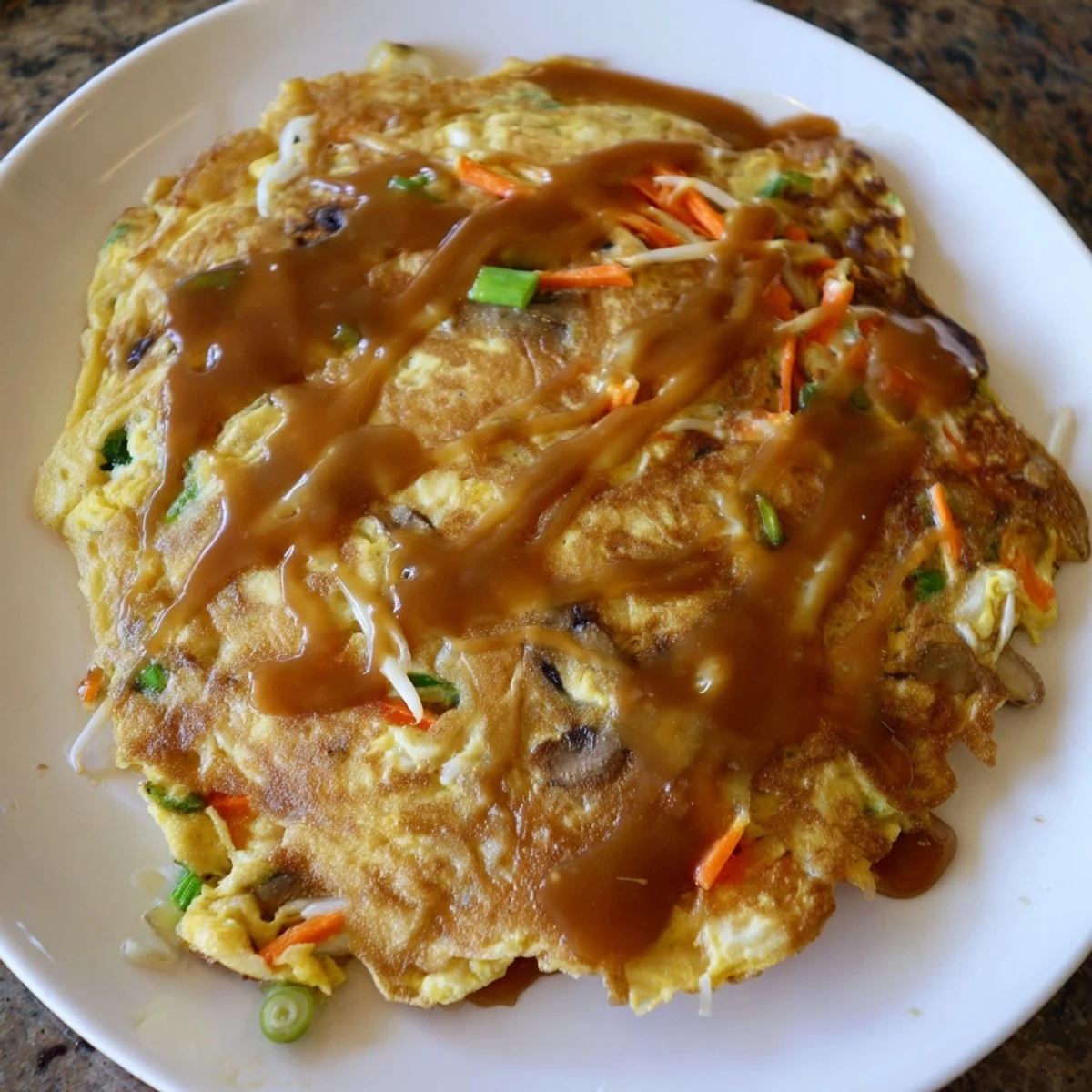 Golden brown crispy Egg Foo Young patties drizzled with savory brown gravy on a white plate