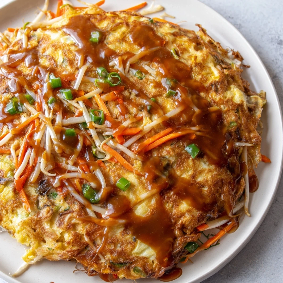 Fluffy vegetable-packed Egg Foo Young omelet fried until perfectly crisp and served with rich sauce