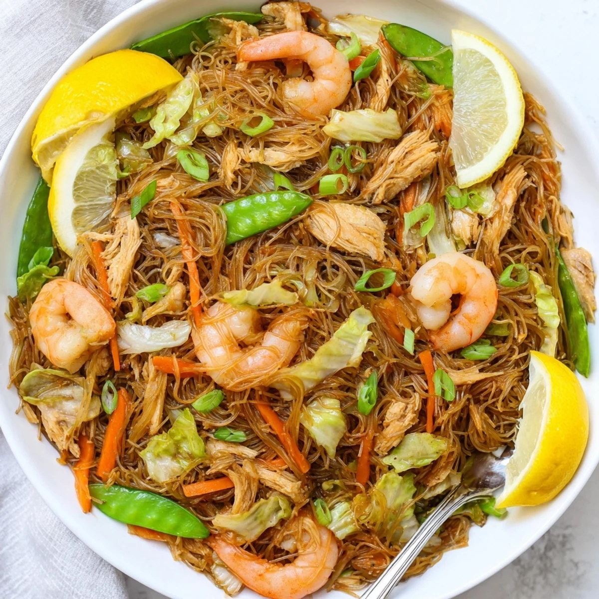 Steamy plate of Traditional Pancit Bihon featuring thin vermicelli noodles tossed with crisp cabbage, carrots, chicken and plump shrimp