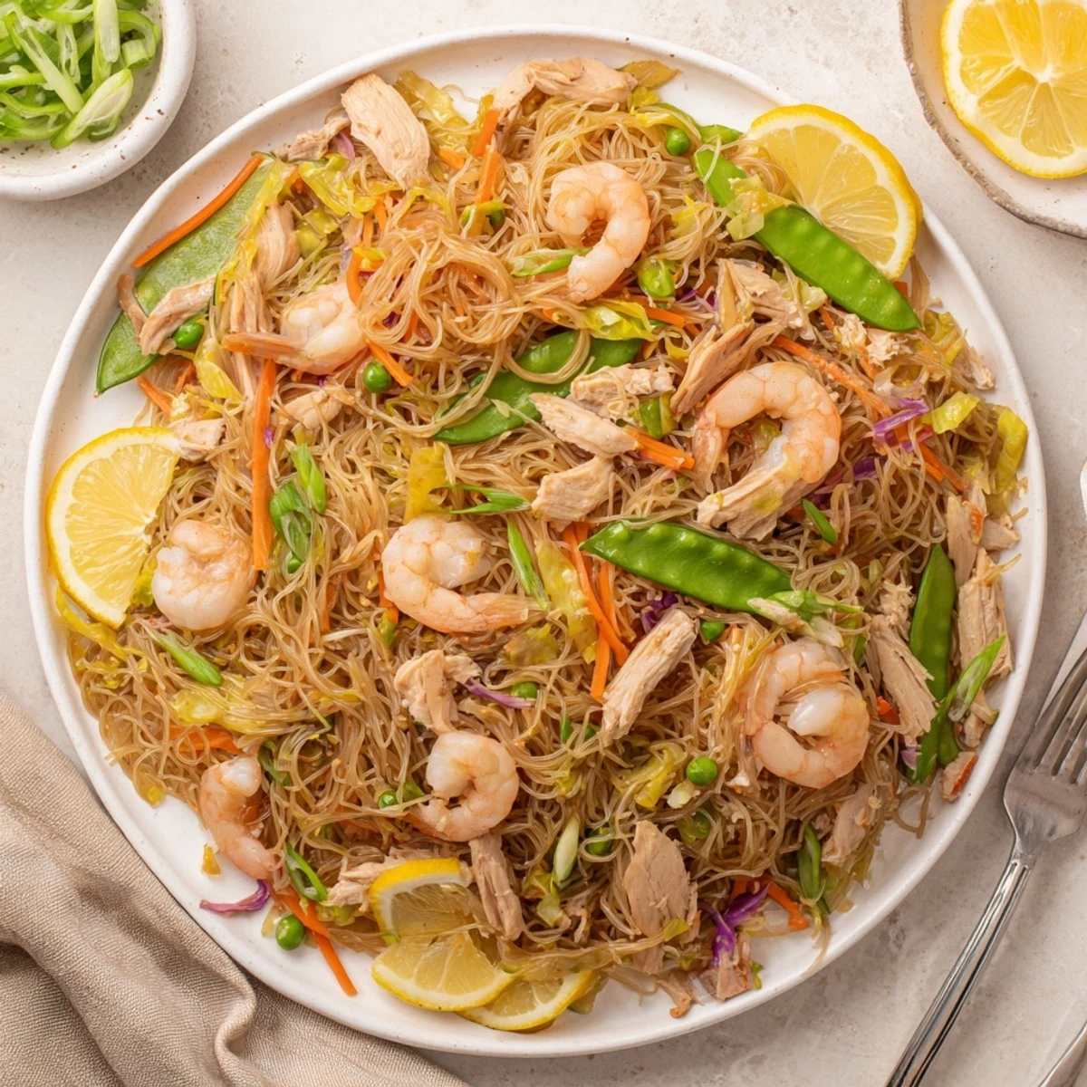 Hearty Traditional Pancit Bihon noodle dish garnished with fresh scallions and lemon wedges, ready for a Filipino family gathering