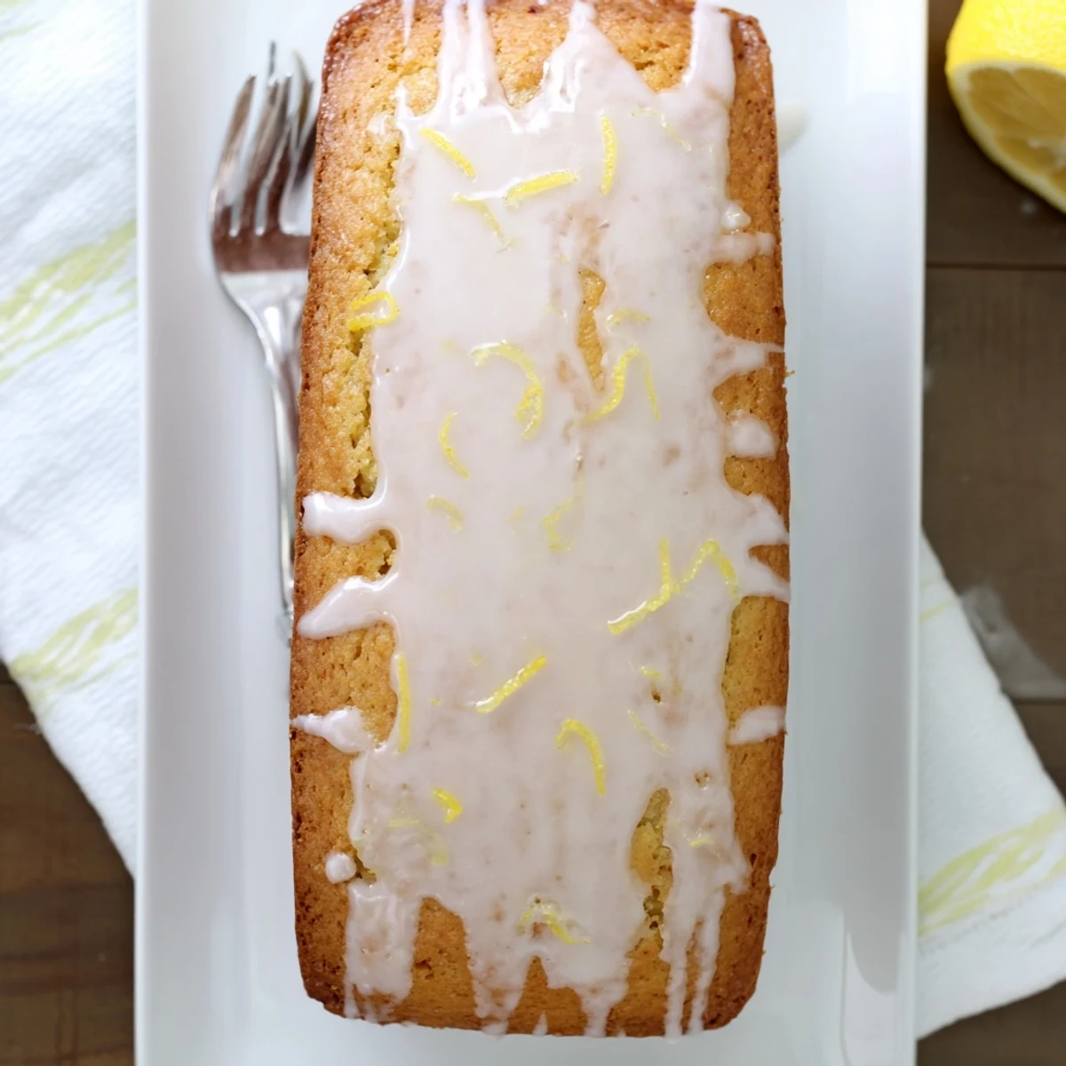 Golden lemon loaf cake drizzled with white citrus glaze on a white serving plate