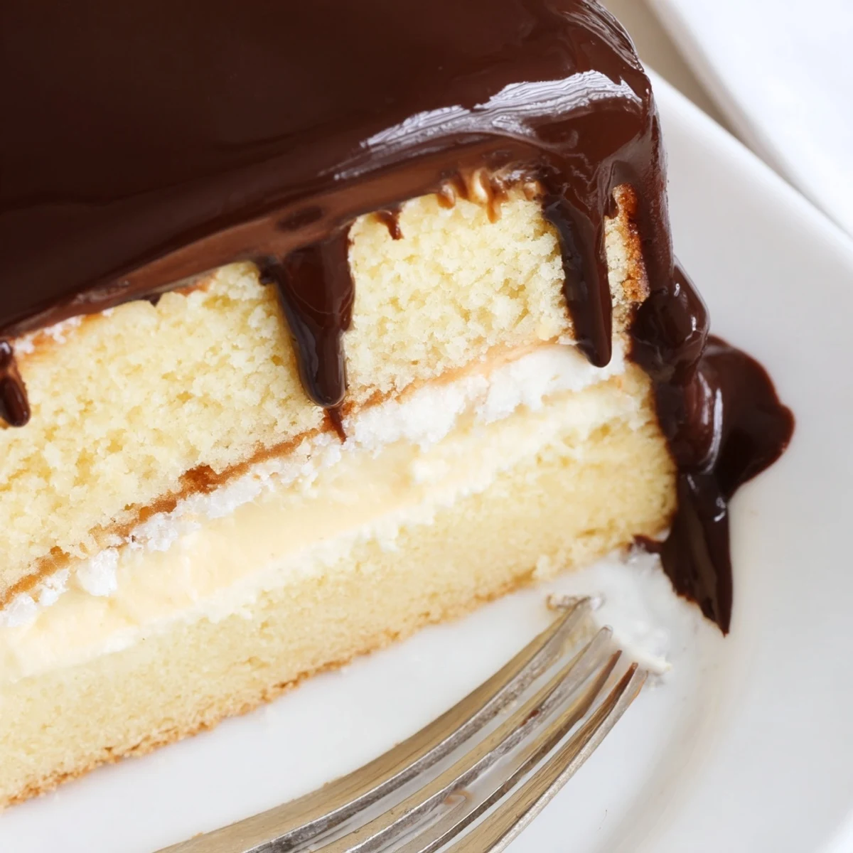 Golden classic Boston cream pie slice showcasing fluffy vanilla cake layers with rich pastry cream filling and smooth chocolate ganache glaze