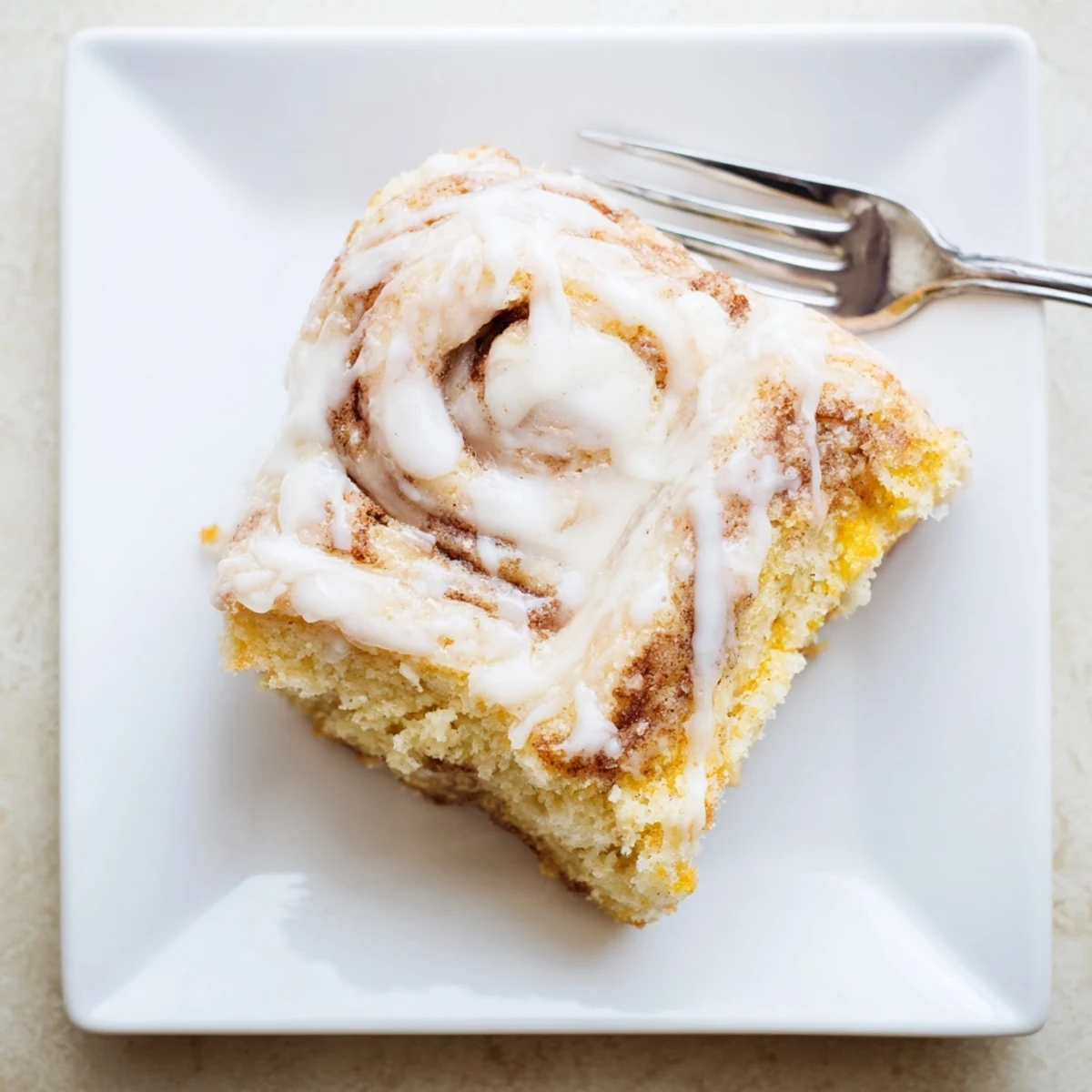 Golden cinnamon roll cake slice topped with silky vanilla glaze on a white plate
