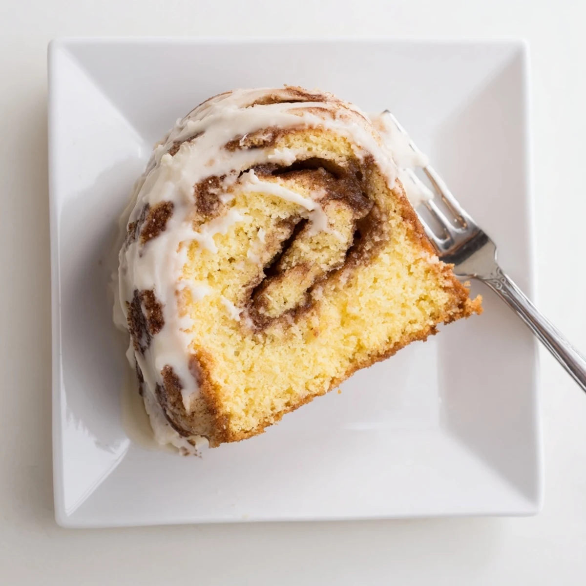 Moist breakfast cake featuring swirling cinnamon-sugar ribbons beneath a sweet white glaze drizzle