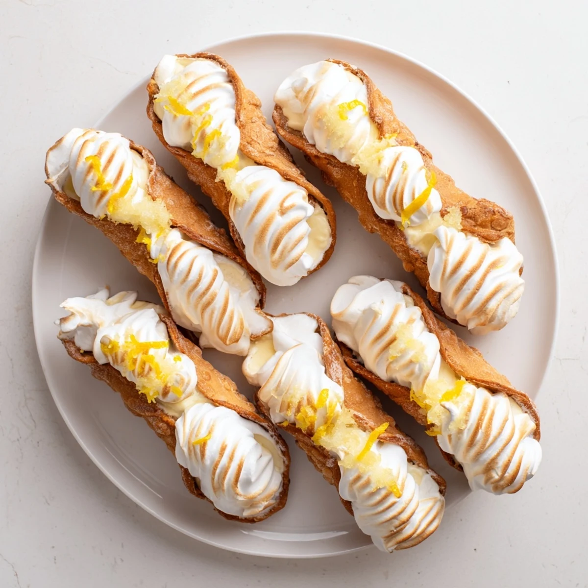 Golden brown cannoli shells piped with zesty lemon cream and toasted meringue peaks