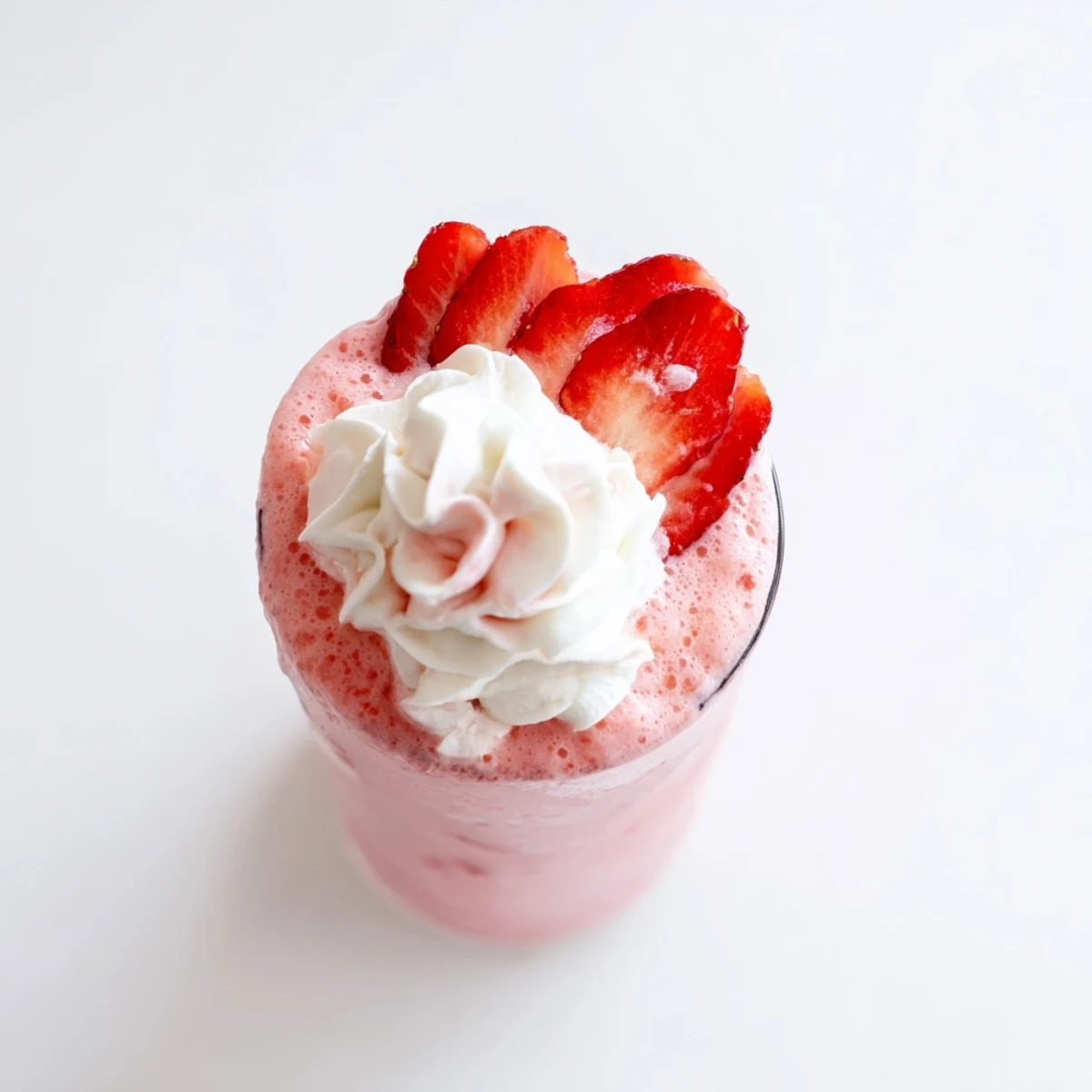 Tall glass filled with pink refreshing strawberry cream frappuccino topped with fluffy whipped cream and fresh strawberry slices