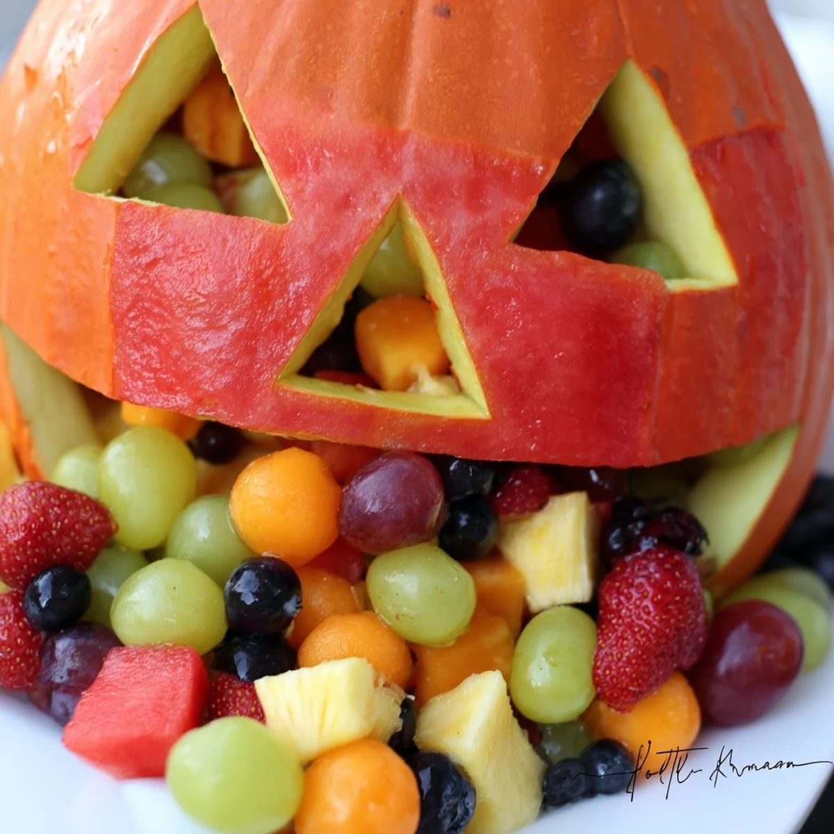 SpookyCarved watermelon Jack O Lantern bowl overflowing with vibrant mixed fresh fruit salad perfect for Halloween parties and summer gatherings