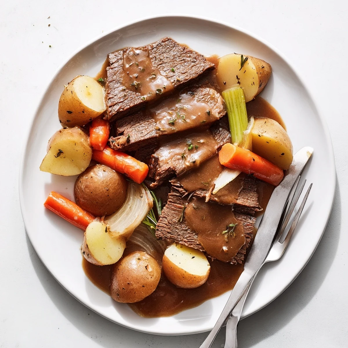 Fork-tender Southern style pot roast served on white platter with caramelized vegetables and savory dark sauce dripping
