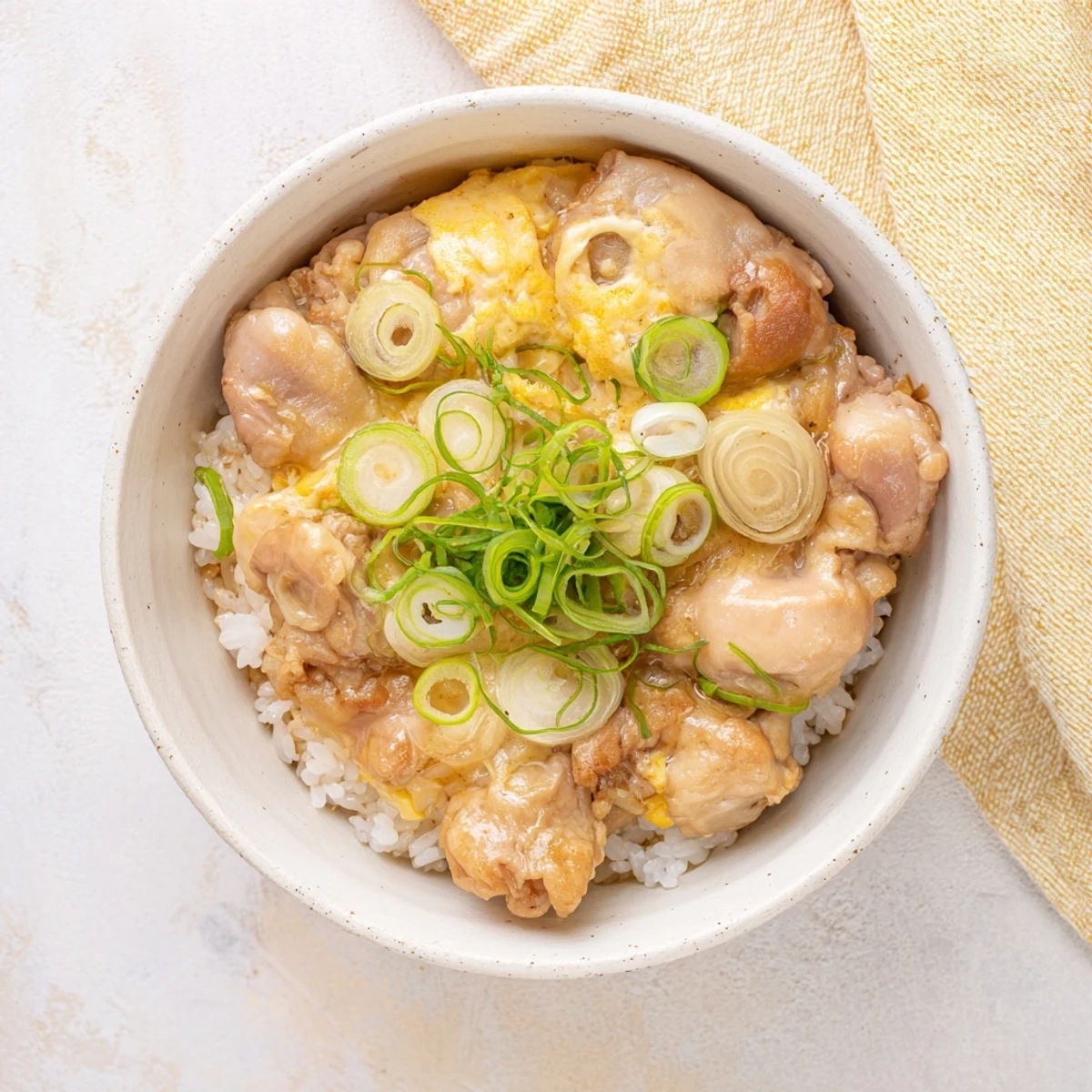 Japanese Oyakodon simmered in savory dashi soy sauce with sliced onions and spring onion garnish