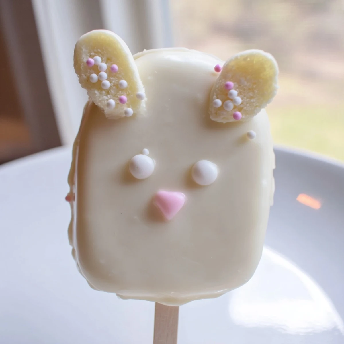 Adorable white chocolate bunny cakesicles with candy eyes and pink ears on wooden board