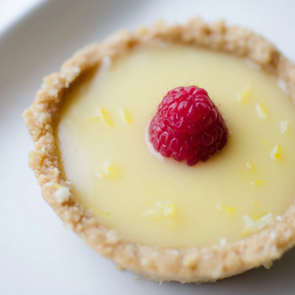 Creamy vegan lemon tarts in crisp almond crusts garnished with delicate lemon zest curls