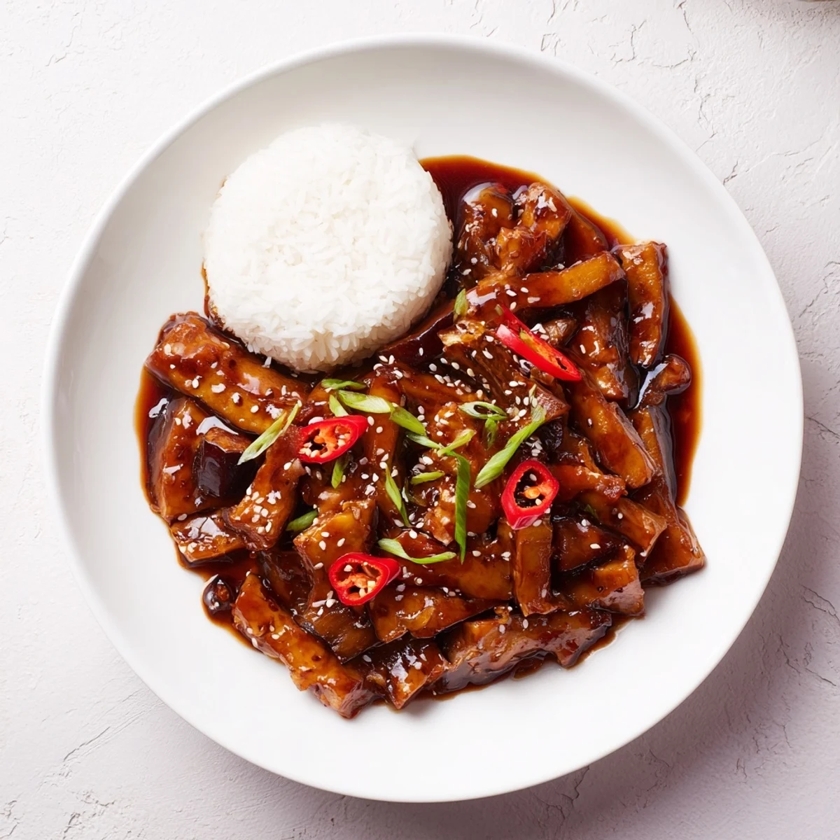 Sichuan Style Braised Aubergines glistening in spicy red sauce, garnished with scallions.