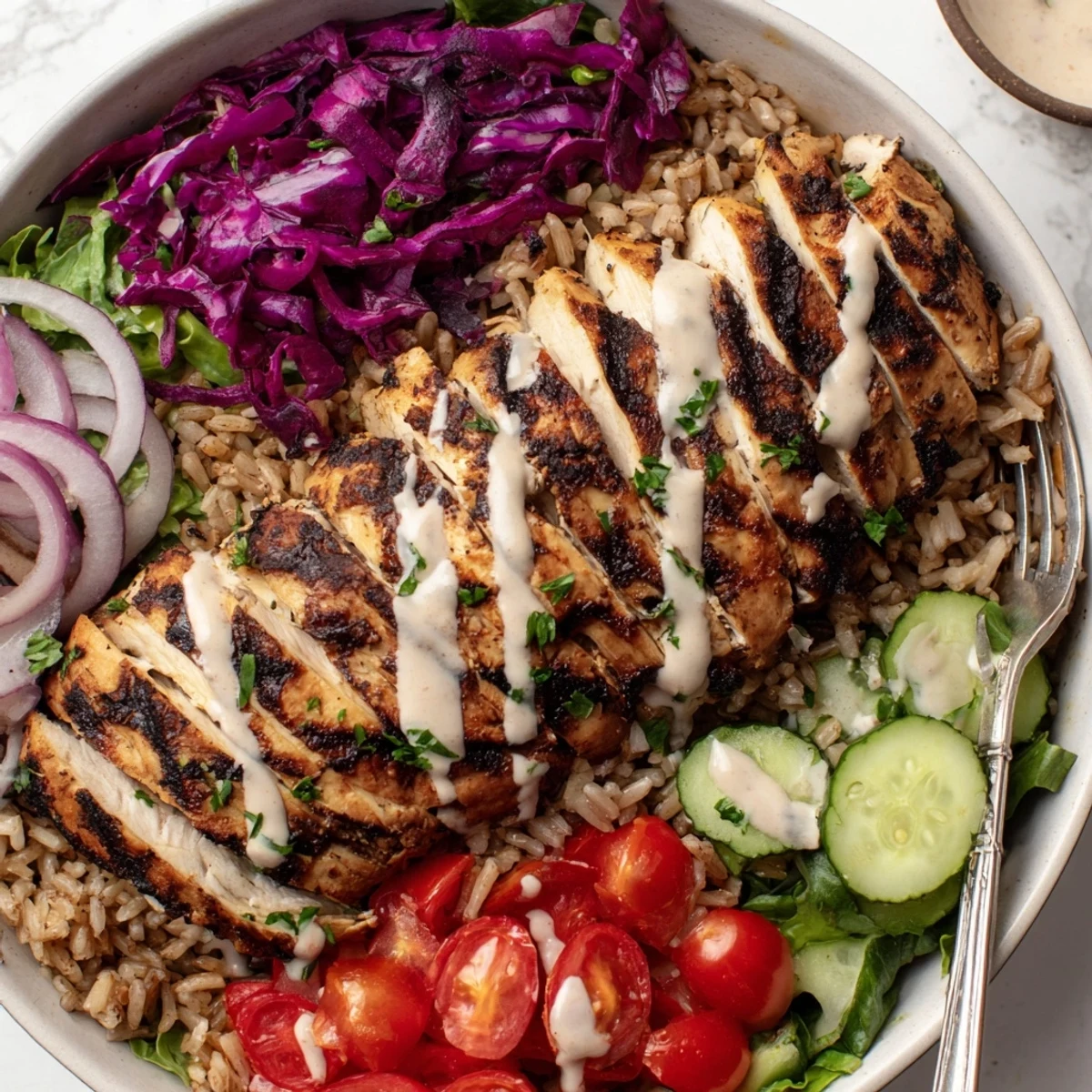 Vibrant lunch bowl featuring marinated chicken with fresh crisp veggies and creamy tahini yogurt sauce drizzle