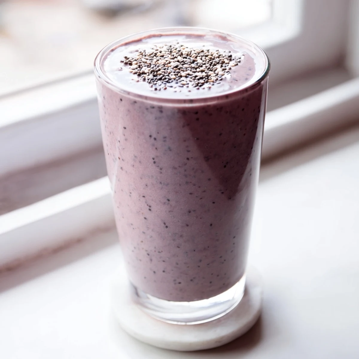 Thick purple chia seed smoothie poured into a glass topped with fresh berries and banana slices
