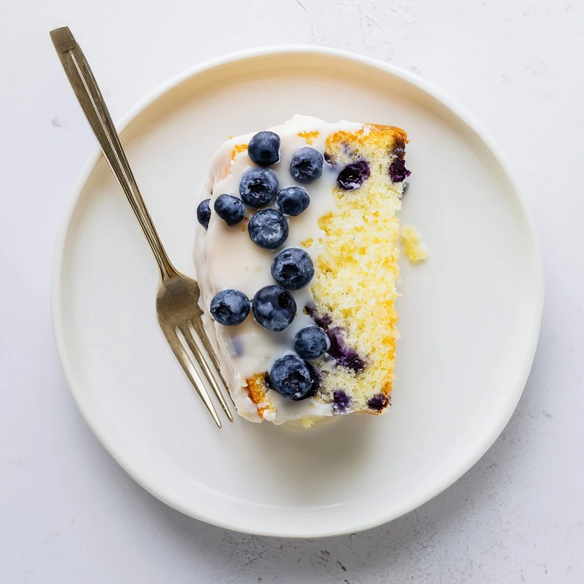 Golden lemon blueberry cake drizzled with white glaze and studded with purple berries