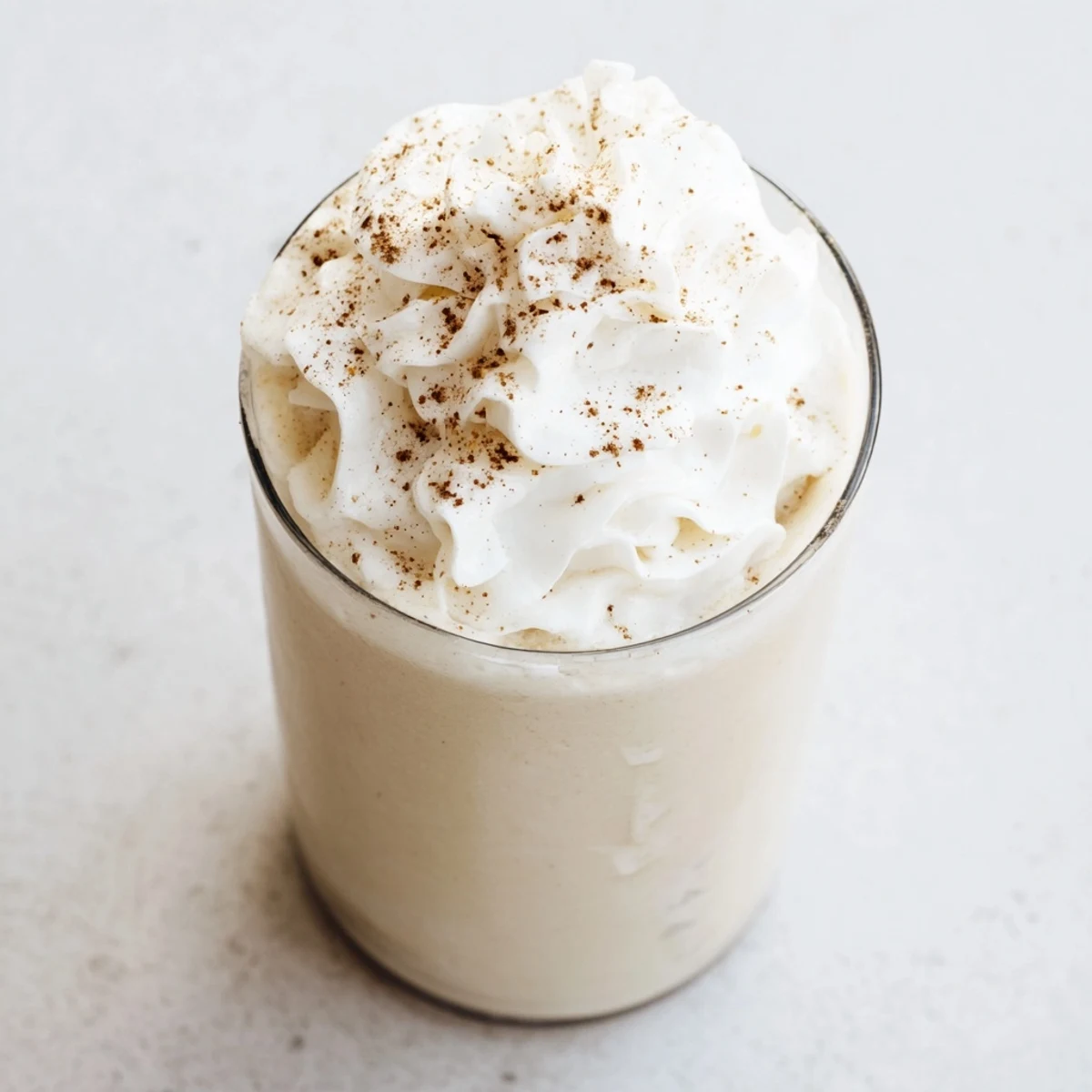 Creamy keto eggnog topped with whipped cream and dusted with ground nutmeg in a clear glass