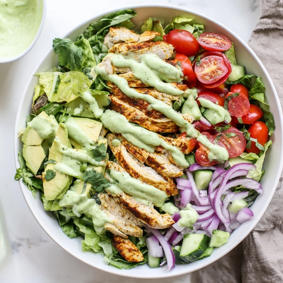 Colorful bowl of creamy avocado grilled chicken salad with fresh vegetables and tangy green dressing drizzled on top