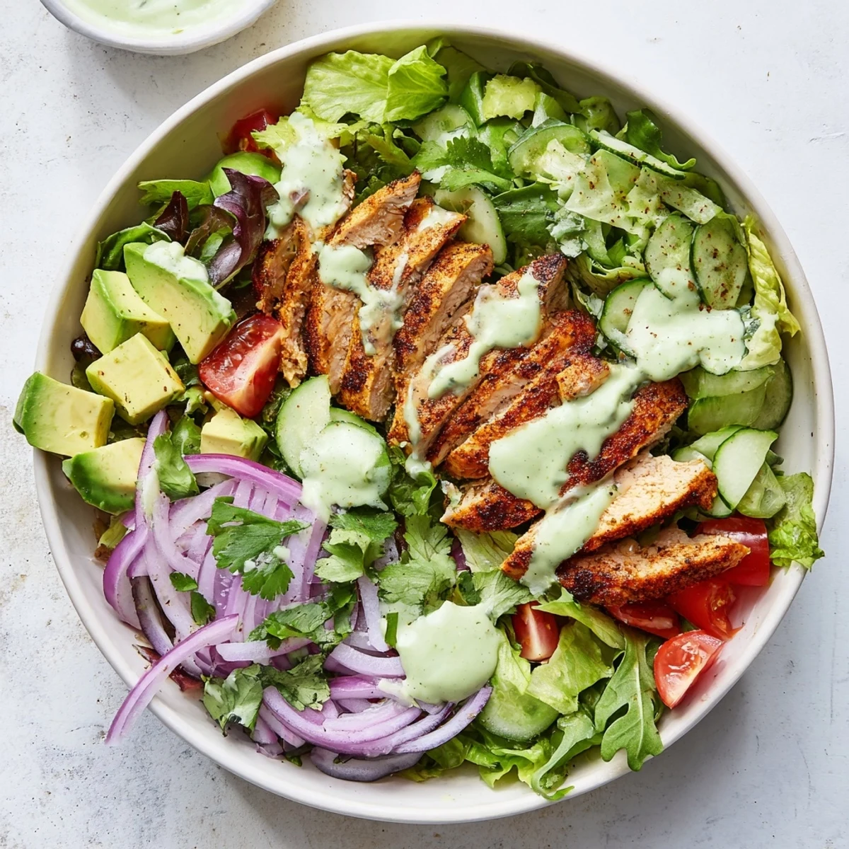 Protein-packed avocado grilled chicken salad bowl featuring tender spiced chicken, cherry tomatoes, cucumber, and rich lime avocado dressing