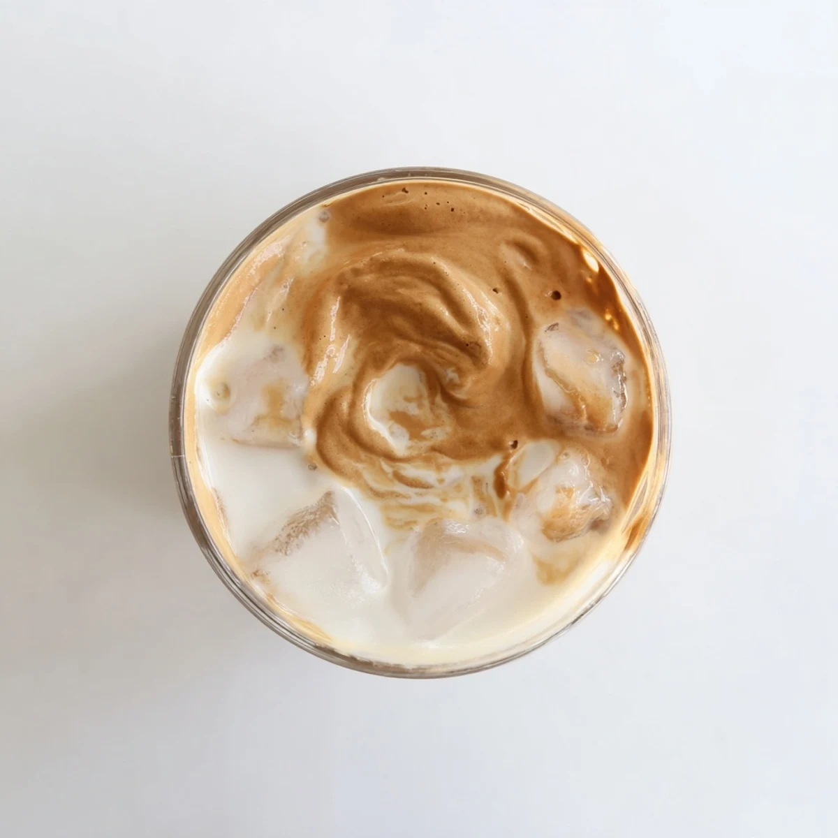 Creamy Dalgona Coffee drink with golden brown whipped foam swirling into white milk below