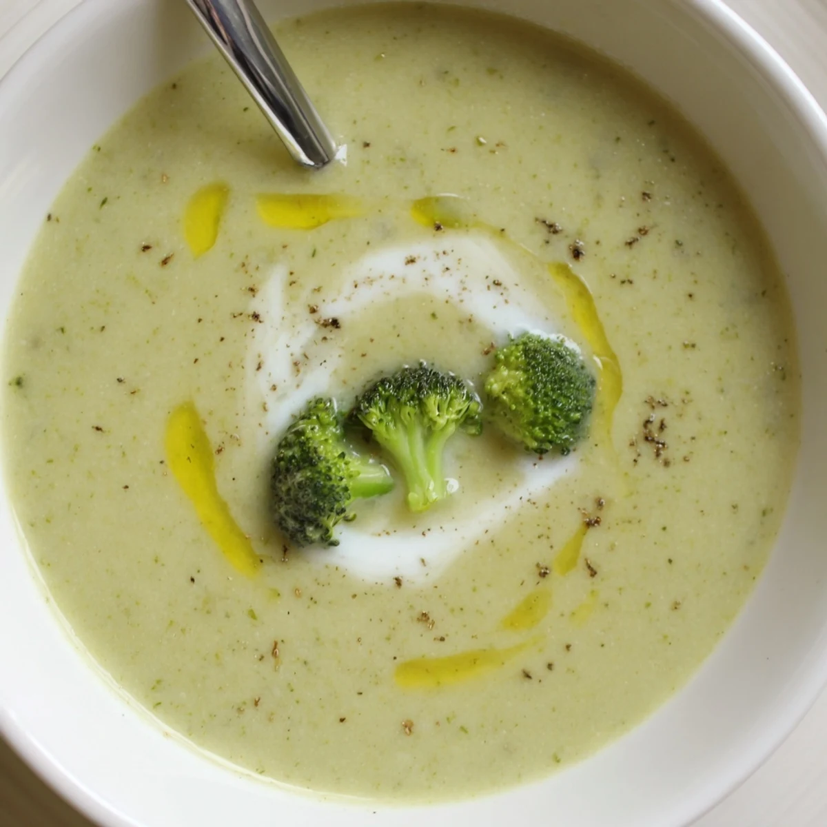 Creamy Broccoli Soup steaming in white bowl, garnished with cream swirl