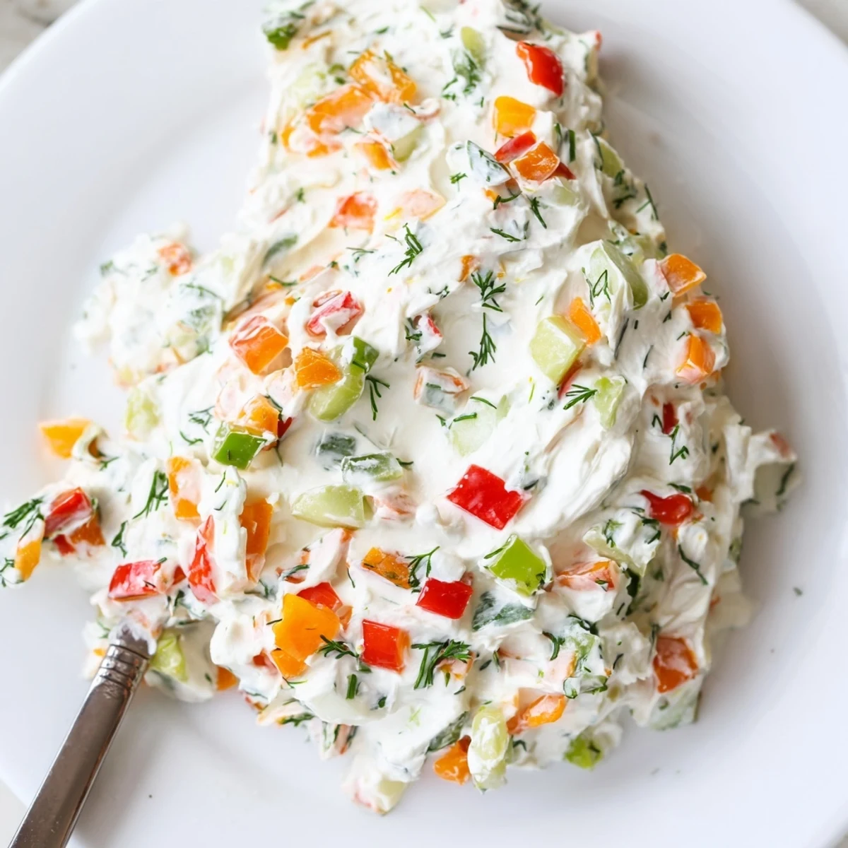 Creamy garden vegetable spread topped with colorful diced peppers and fresh herbs on a white serving plate