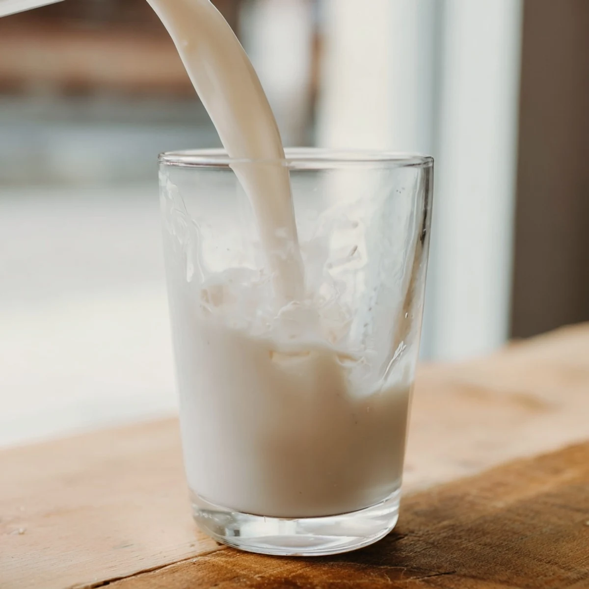 Pouring creamy white almond milk from glass pitcher into clear drinking cup
