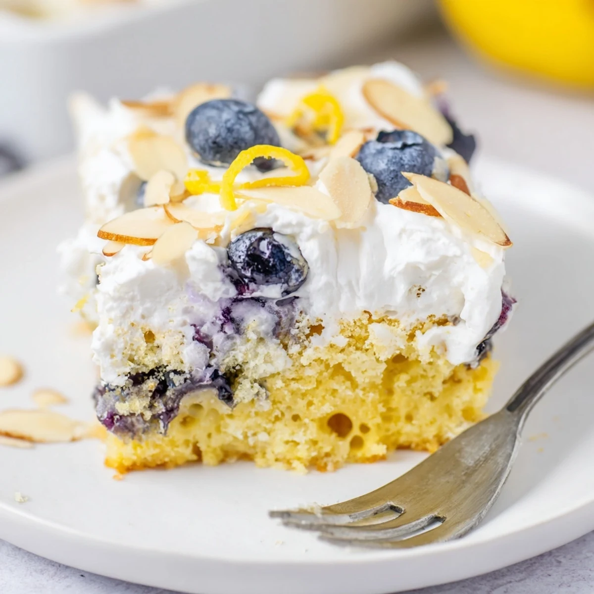 Creamy whipped frosted lemon blueberry poke cake garnished with golden almonds and fresh blueberry accents