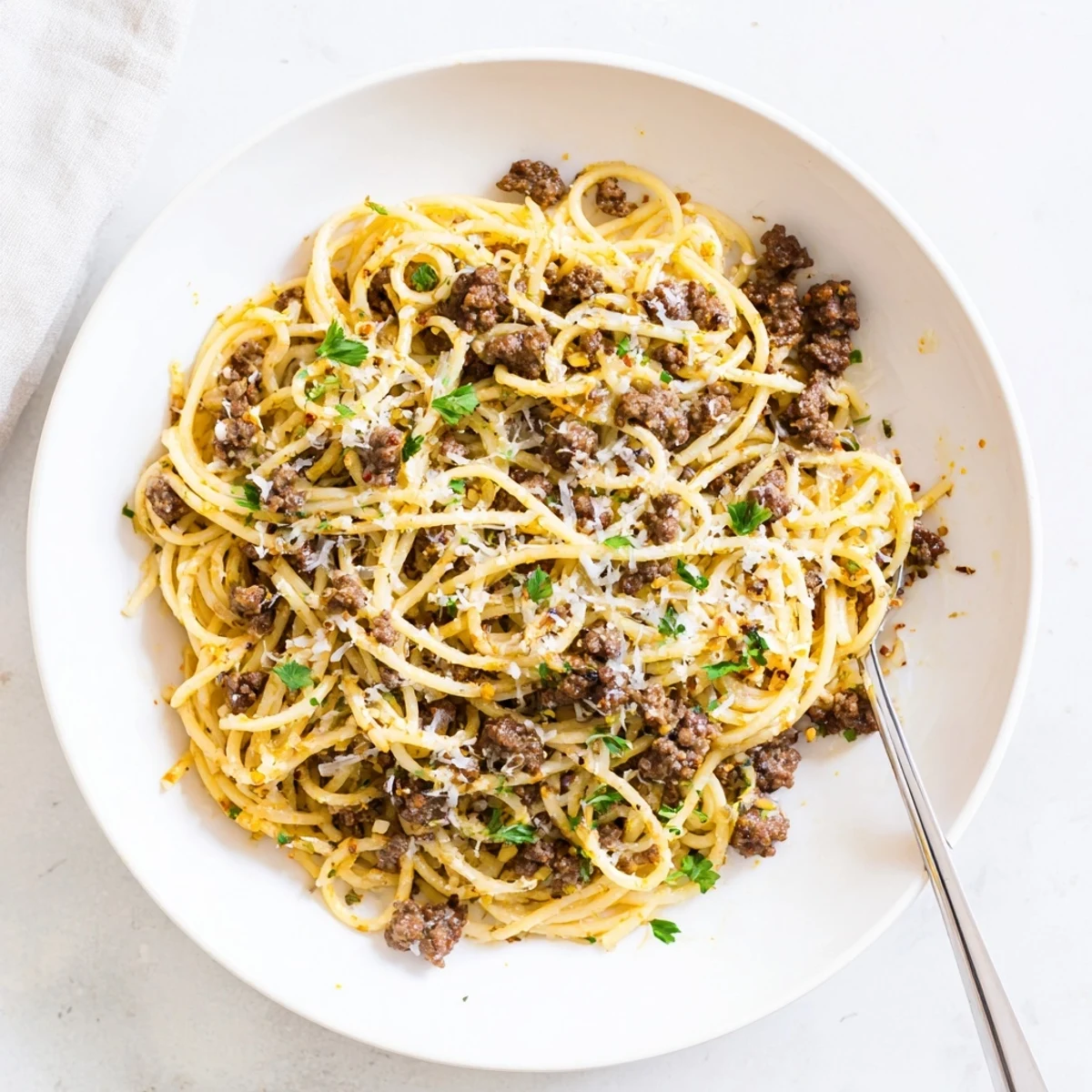 Steaming plate of garlic butter pasta with ground beef topped with fresh parsley