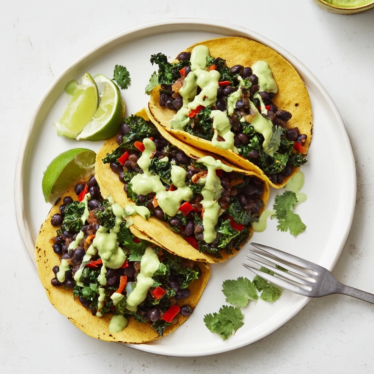 Smoky black bean kale tacos drizzled with vibrant creamy green sauce on soft tortillas