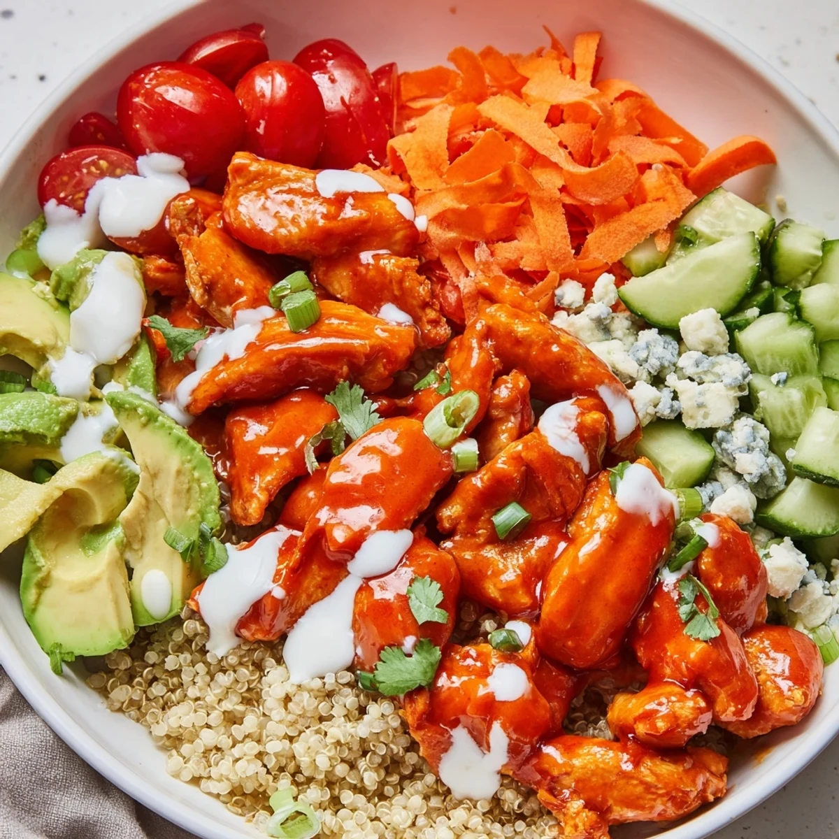 Colorful buffalo chicken grain bowl loaded with shredded carrots tomatoes and crumbled blue cheese