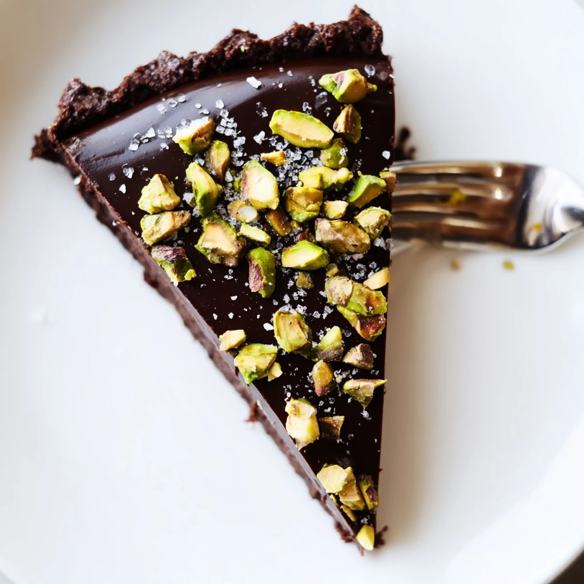 Velvety Dark Chocolate Pistachio Tart garnished with sea salt and vibrant nuts on a ceramic plate