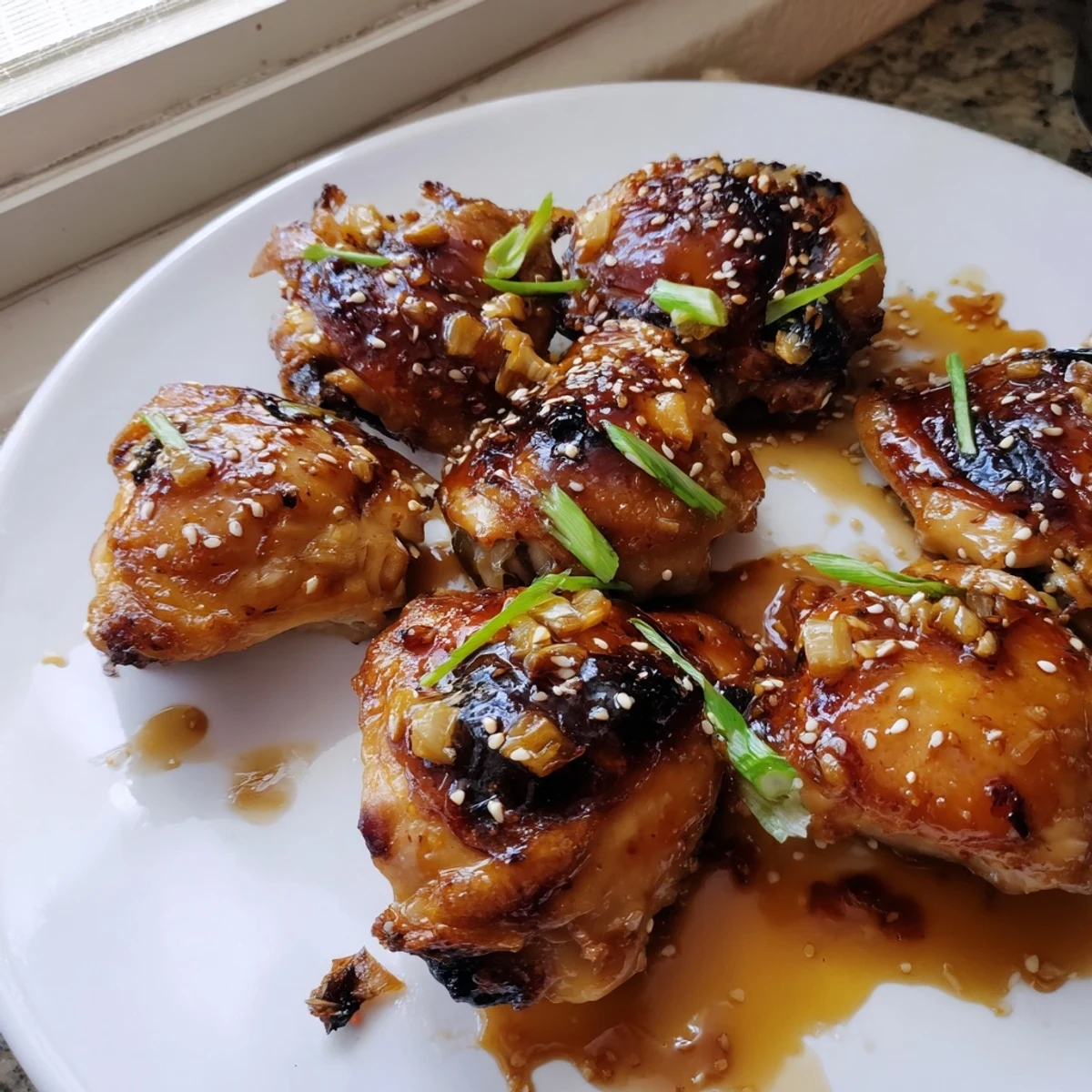 Juicy ginger garlic chicken thighs garnished with green onions and sesame seeds on a white platter