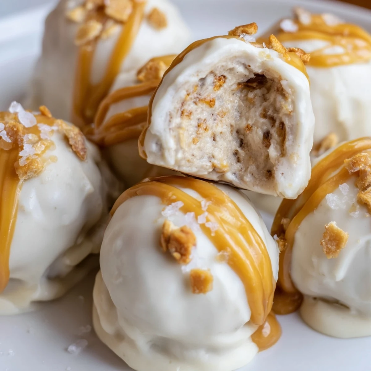 Creamy salted caramel pretzel cheesecake balls drizzled with golden caramel on a rustic tray
