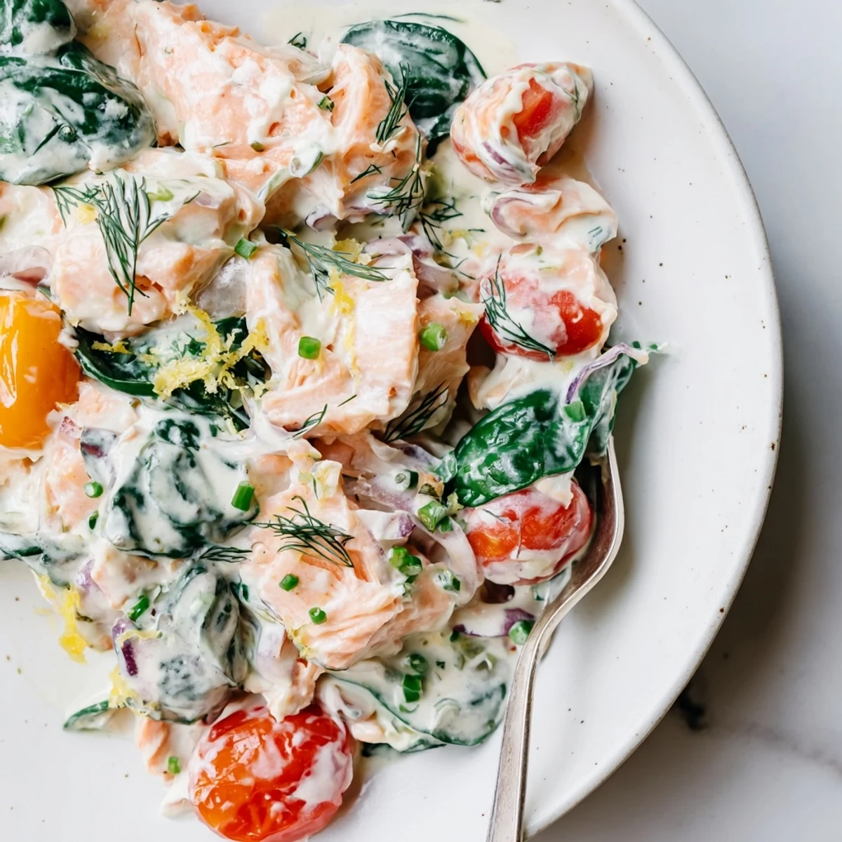 Creamy leftover salmon recipe served in a skillet with spinach, tomatoes, and fresh dill